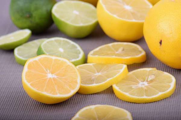 Several thin yellow lemon slices and a few green lime slices, and a whole lemon and lime, on a gray background