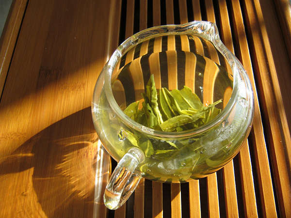 Large green tea leaves steeping in a glass pitcher, on a wooden grate