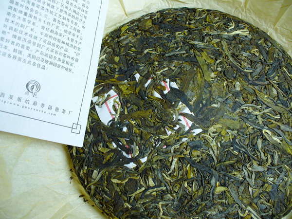 Round, compressed tea cake with varying shades of green leaf, pamphlet with Chinese characters on left
