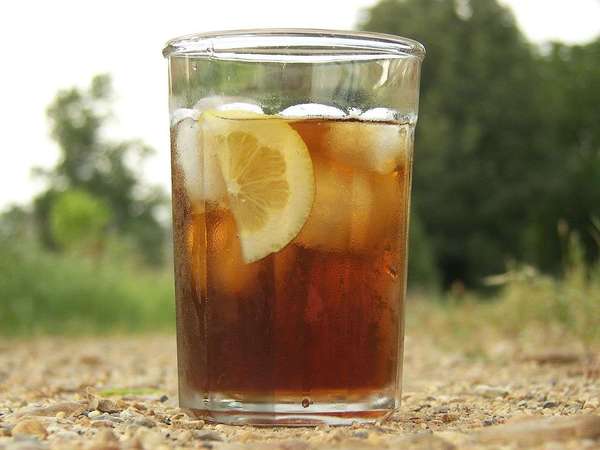Large glass of iced black tea with lemon and ice cubes, on gravel with blurred green background