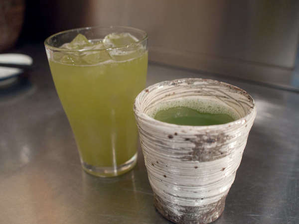 Ceramic cup with hot green tea on right, glass of iced green tea on left, paler yellow in color