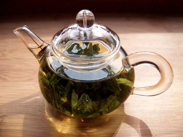 Glass teapot filled with large-leaf green tea leaves, on wooden background