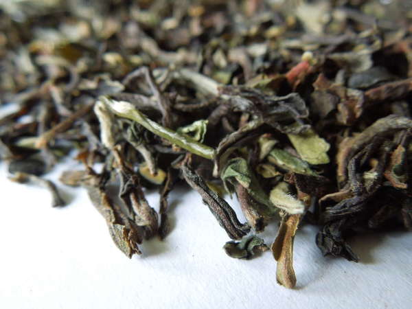 Loose-leaf tea with irregular, crinkly leaves, colors ranging from pale green through orange and olive to dark brown or black