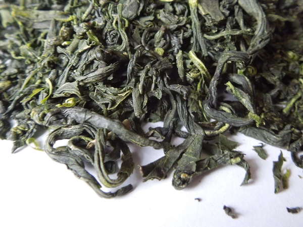 Loose-leaf green tea with irregularly curvy and wrinkly leaves, vibrant green color, some bright yellowish-green, others dark forest green
