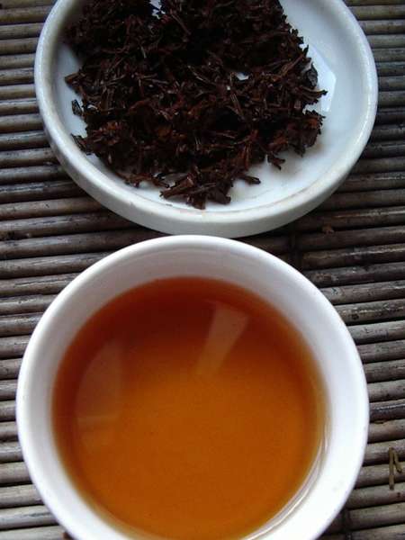Cup of brewed black tea below, wet (used) black tea leaves on dish above