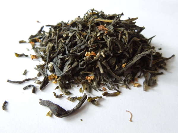 Tea with dark olive-green leaves, many broken, and a few small orange dried flowers mixed in