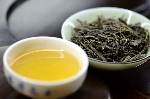 Cup of yellow-colored tea on left, dish of gray-green tea leaves on right