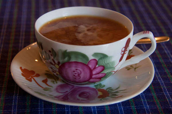 Black tea with swirling milk in a rose-patterned teacup on matching saucer, on blue plaid tablecloth