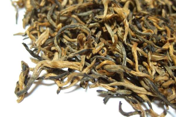 Loose-leaf tea with mostly golden-orange, intact leaves, slightly twisty, some black/brown leaves in the mix