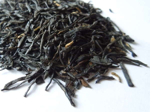 Loose-leaf black tea with long, wiry black leaves and a few golden tips