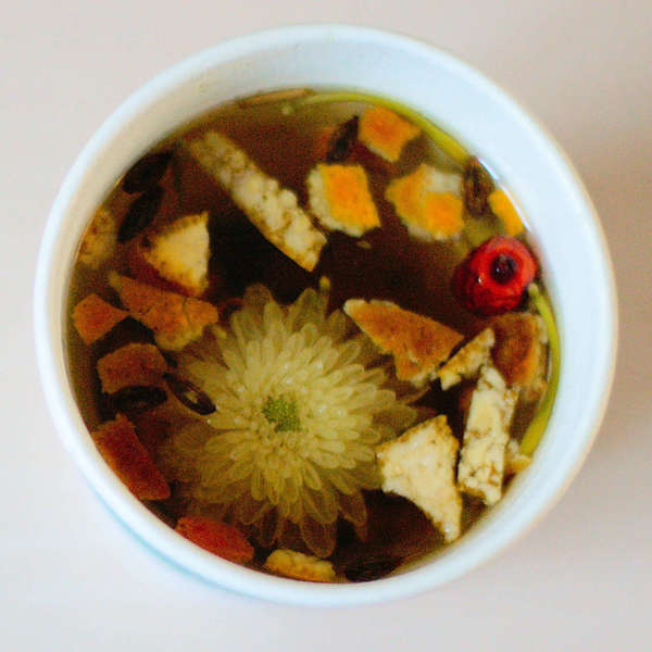 Flowers and citrus peel steeping as a dark brown herbal tea in a white cup