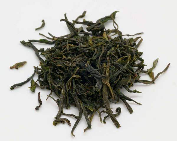 Loose-leaf green tea with long, wiry, dark green leaves with golden hints, on white background