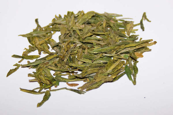 Loose-leaf green tea with long, flat, yellow-green leaves on a white background