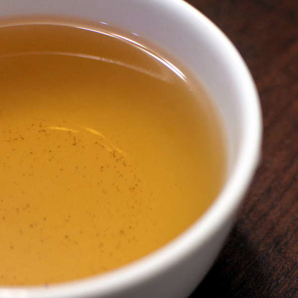 Golden-yellow tea in white teacup on dark wooden background