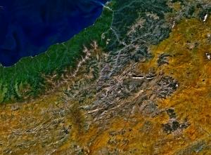 Satellite photo showing water in the top left, a green area, and mountains followed by a drier area to the southeast.