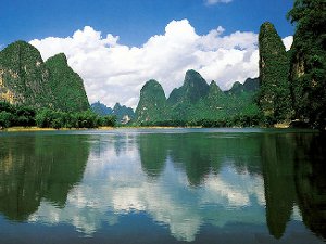 A river with tall, round-top mountains rising behind it