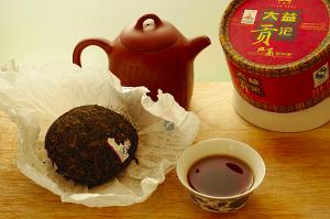 A pu-erh cake, teapot, packaging, and a cup of tea showing a dark brown color
