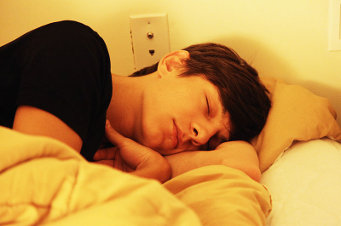 A person sleeping on nondescript fluffy white bedding with yellow lighting