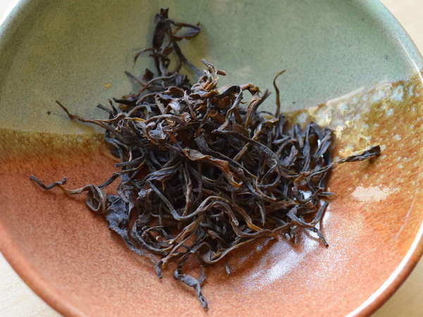 Loose-leaf tea with long, intact, wiry and curvy leaves, brown to olive-reddish, in ceramic bowl