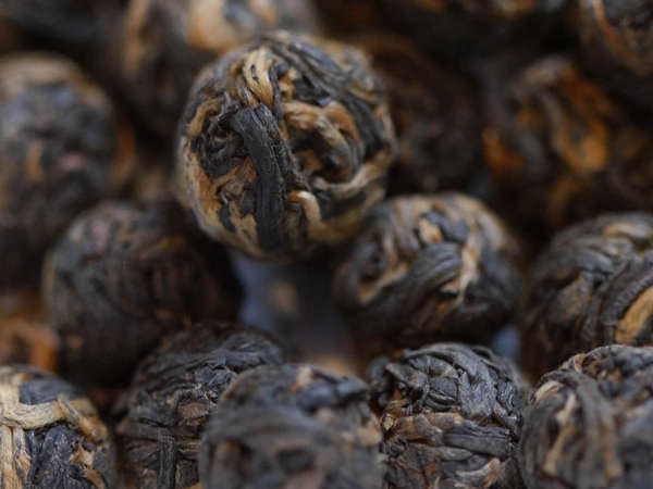 Black tea leaves tightly rolled into spheres, showing mostly black leaves with some golden orange