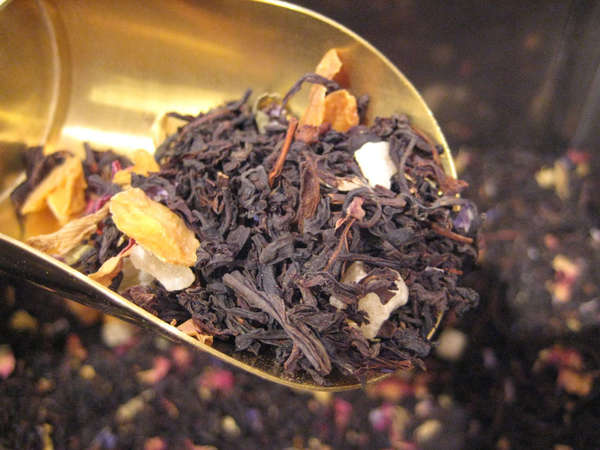 Loose-leaf black tea and dried fruit pieces in a brass-colored scoop