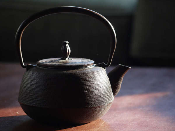 A cast-iron teapot with its handle up, on a plain brown table against a dark background