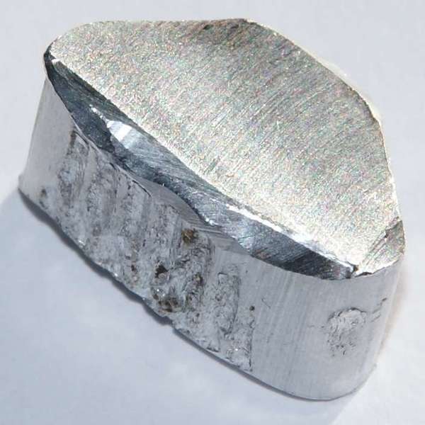 Chunk of aluminum metal, shiny and silvery in color, with rough upper surface