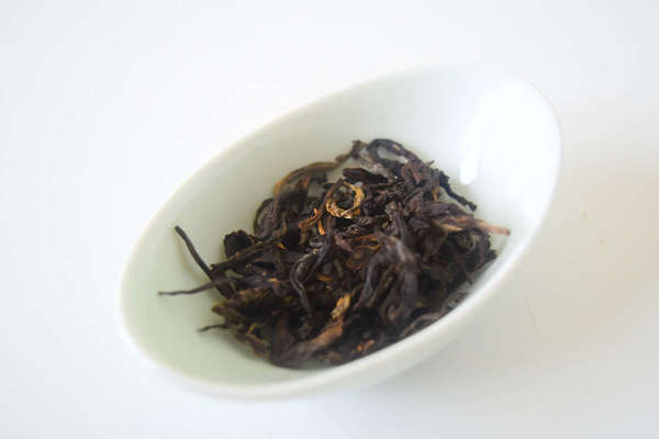 Loose-leaf tea with dark brown and orange colors, long, irregular-shaped leaves,  in ovate white dish against white background