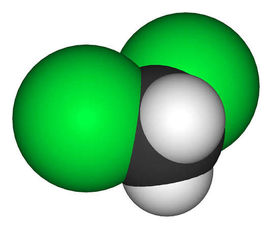 Ball model of dichloromethan molecule, two massive Chlorine atoms on left and right colored green, central carbon atom black, two small hydrogens light gray