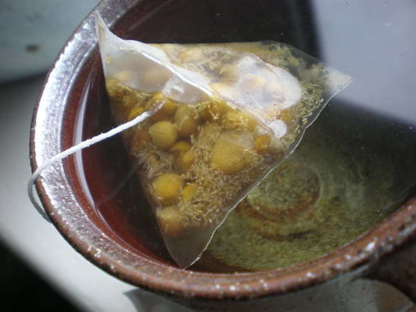 Pyramid sachet of chamomile tea in a brown ceramic cup full of water