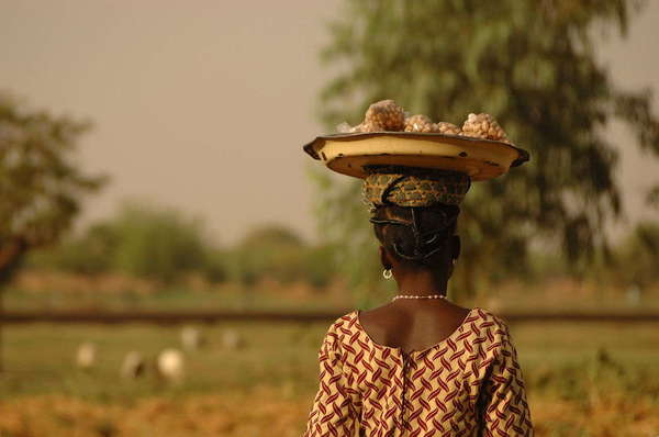 Woman with a wide, flat hat with stacked bags of peanuts in it, in an open landscape with blurred background