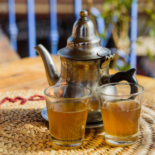 Two small cups of golden-colored tea, metal teapot, on a straw placemat