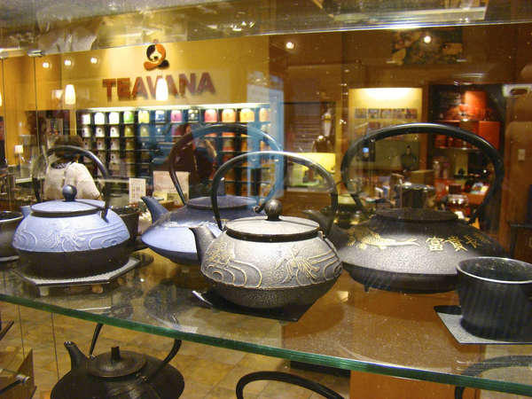 Teapots behind a glass window, in a store display, with Teavana logo and wall of tea tins in the background
