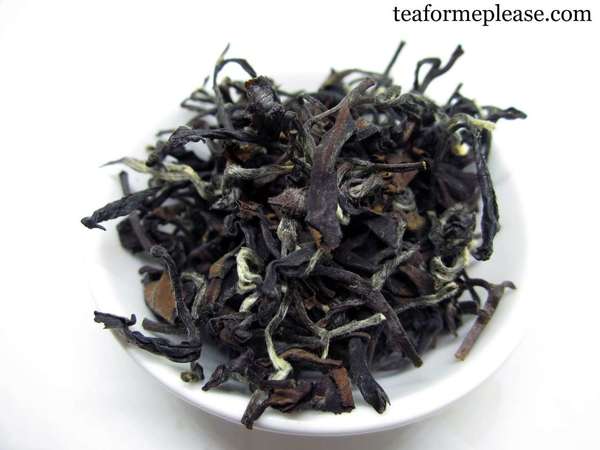 Bowl for of large, curly tea leaves, mostly black, with some silvery downy tips and lighter brown leaves 