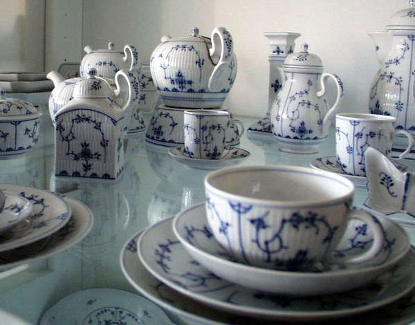 Blue-white porceilain tea set showing teacups, teapots, plates, and saucers of varying sizes, set on display on a glass surface