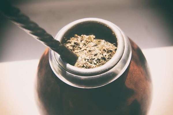 Traditional gourd with metal rim, filled with green yerba mate, with thick metal straw sticking out