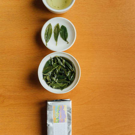 Overhead view of gaiwan filled with steeping green tea, lid placed above with three whole tea leaves spread out