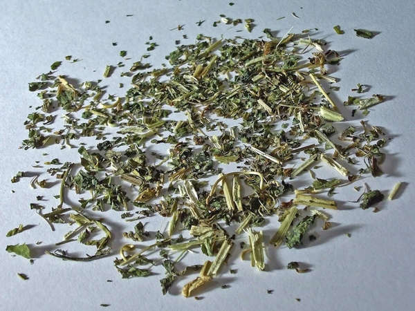 Dried herb with straw-yellow stems and small, dark gray-green leaf pieces, on a white background