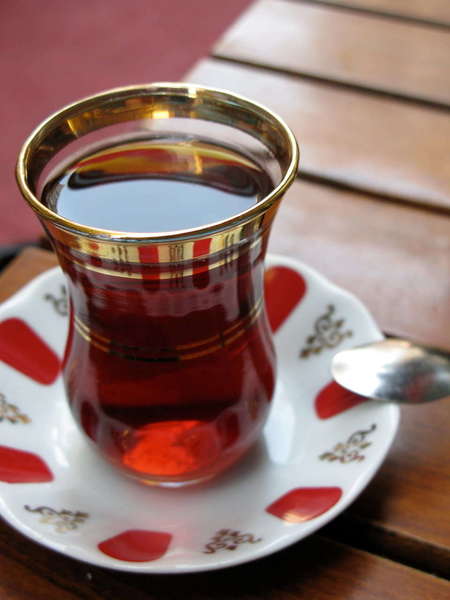 Glass teacup with gold rim, filled with reddish tea liquor, on white saucer with bold red pattern