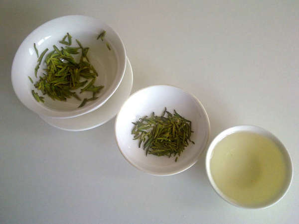 Cup of pale yellow-green tea lower right, dish with loose-leaf green tea center, gaiwan with wet tea leaves top left
