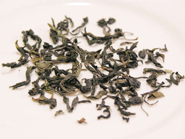 Green, twisted and curved tea leaves, whole and intact, against a white background