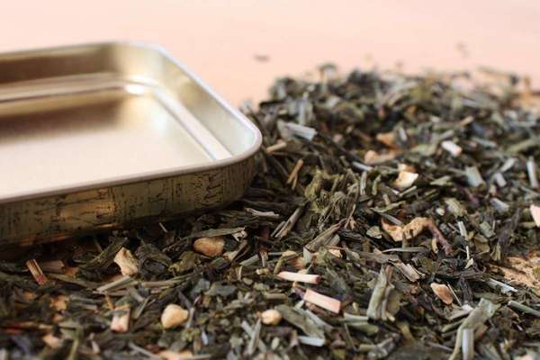 Upside down square metal tea tin lid, loose-leaf dried herbs showing dark gray-green leaf and straw-colored stem