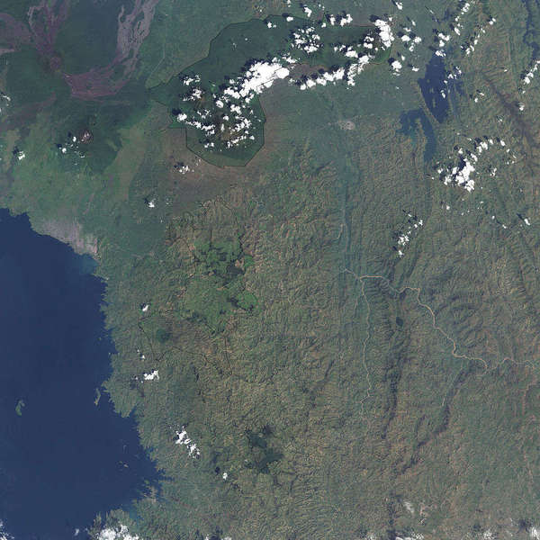 Satellite photo showing a blue lake to the southwest, some hilly terrain, with patches of dark green, lighter green, and olive, a few scattered bright white clouds