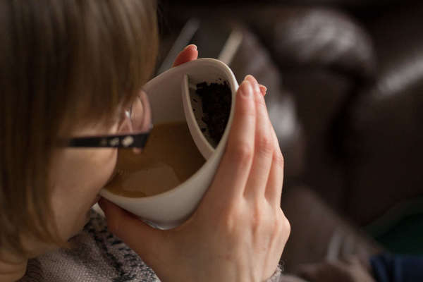 A woman drinking tea from a white ceramic cup with a built-in filter for tea leaves