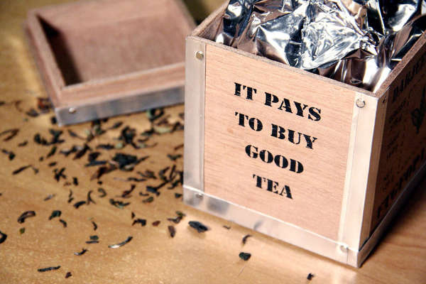 Metal-reinforced wooden crate reading: it pays to buy good tea, with foil bag, and loose-leaf black tea spilled outside