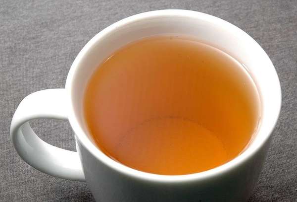 Plain white teacup on gray background, showing golden-orange color to the brewed tea