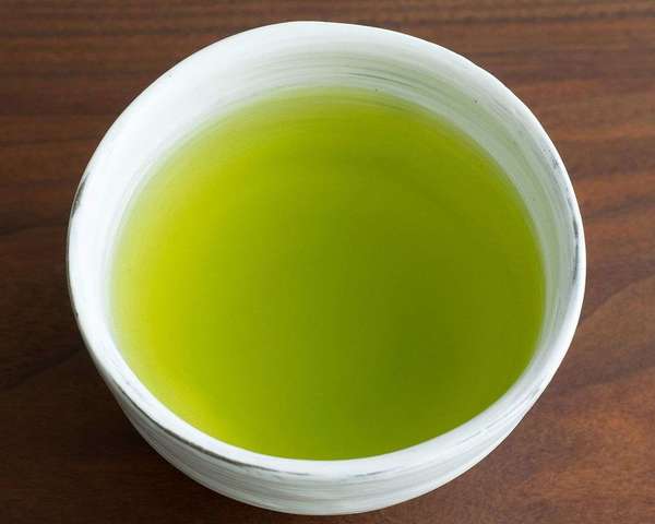 White cup full of tea with intense green color, yellower around the edges