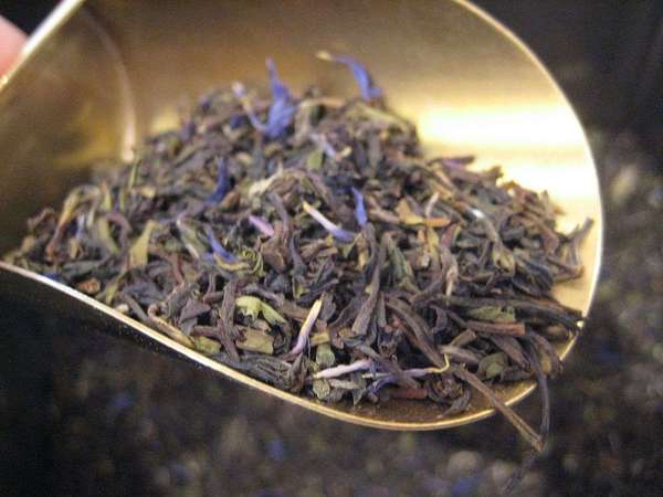 Loose-leaf tea with brown to gray-green leaf, and blue flowers mixed in, in a brass-colored scoop