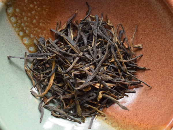Loose-leaf tippy black tea with long, narrow, straight needle-shaped leaves, and golden-orange buds