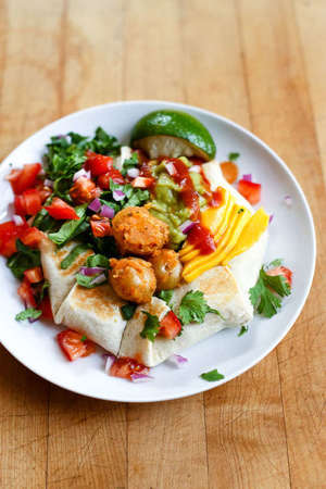 White plate with food with numerous diverse vegetables and herbs in vibrant colors: red, green, yellow, off-white